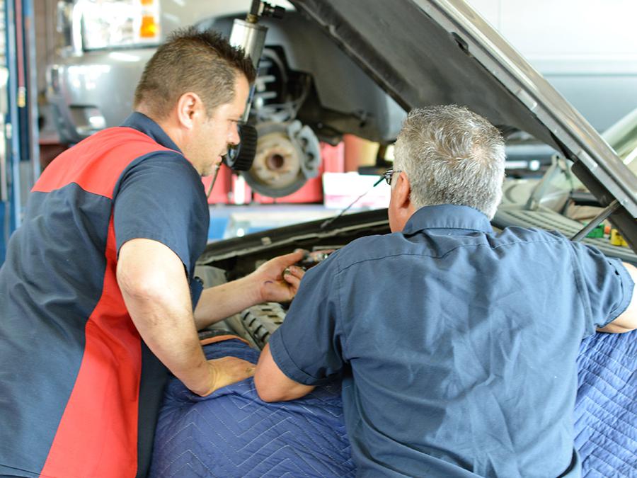 Two men are working on a car with the hood open