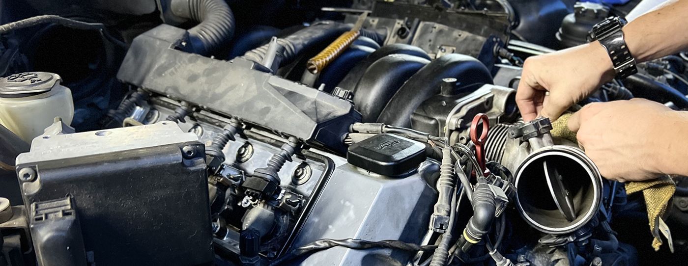 Hands working on a car engine with exposed hoses and parts in a garage