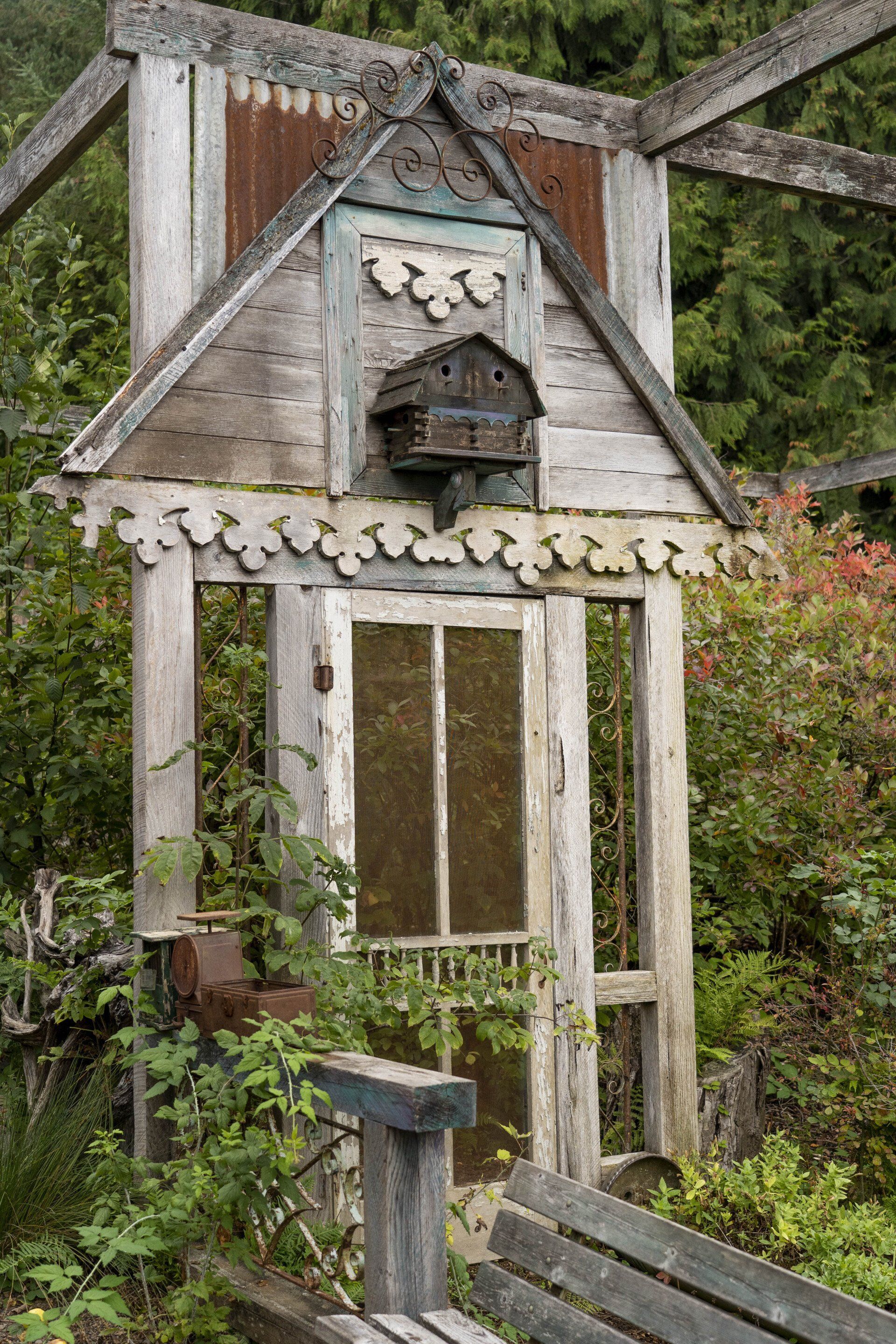 Weathered wooden structure with a small birdhouse on the roof, fronted by a bench. 