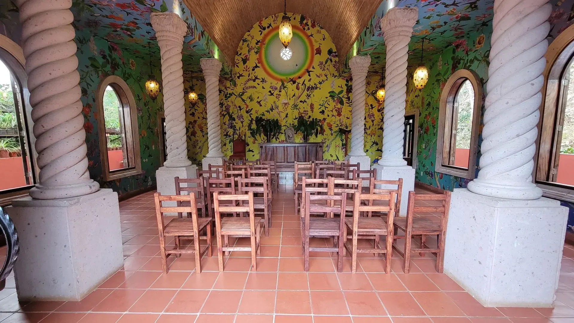 An ornate, colorful chapel interior with rows of wooden chairs facing an altar.