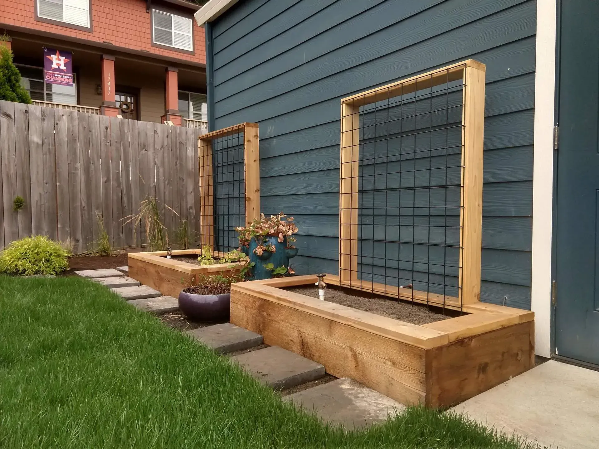 Two wooden planter boxes with metal trellises against a blue house. 