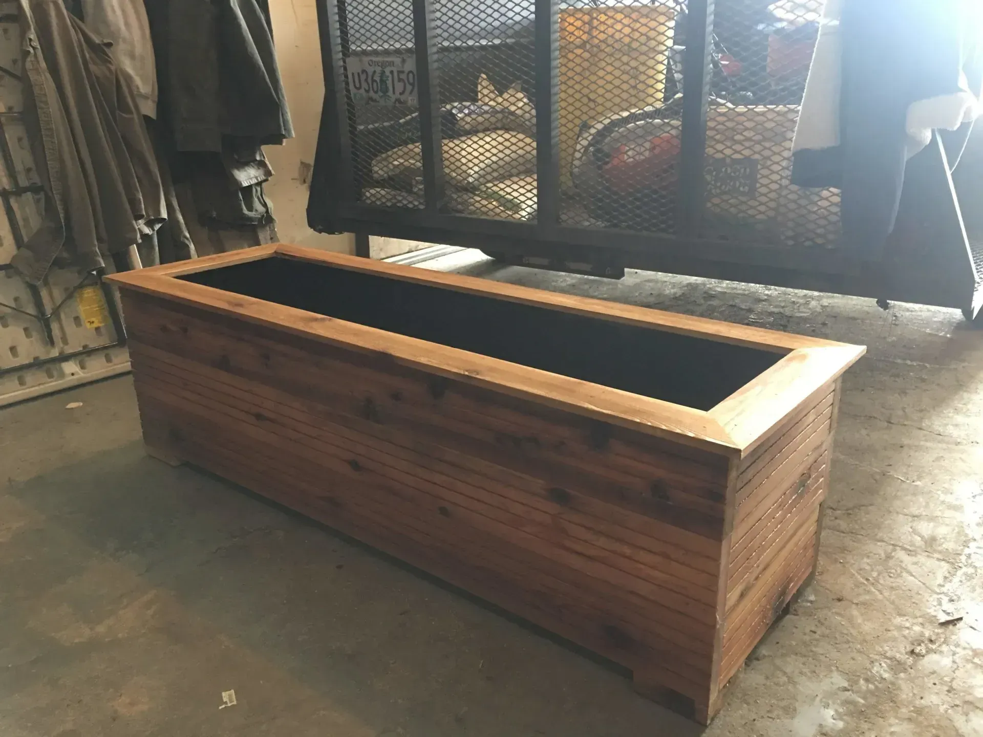 Wooden rectangular planter box with a dark interior, sitting on a concrete floor. 
