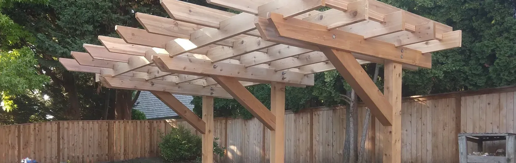 Wooden pergola in a backyard setting with a wooden fence and green trees. 