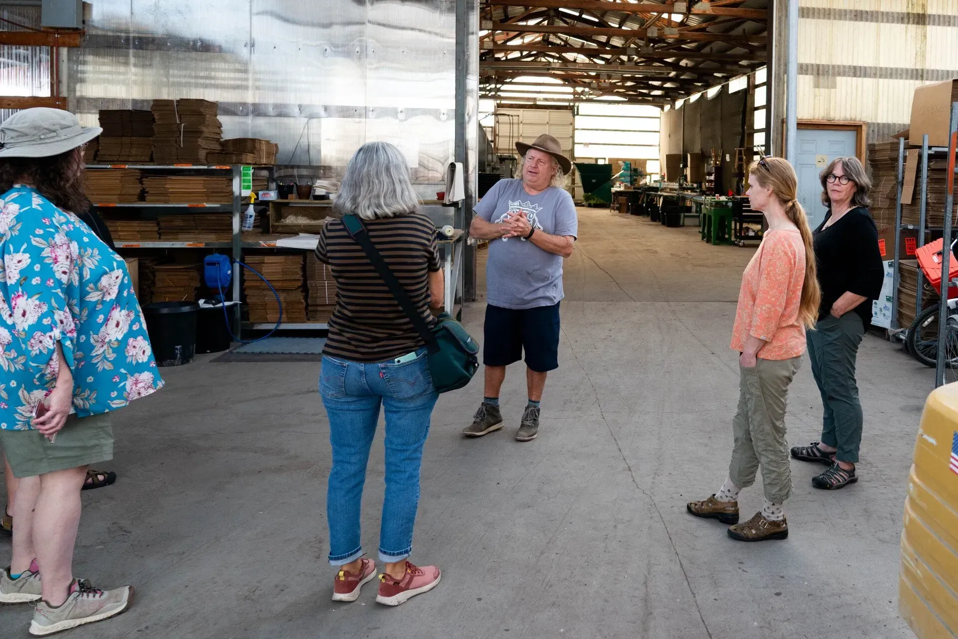 A group of people listens to a man gesturing inside a warehouse. 