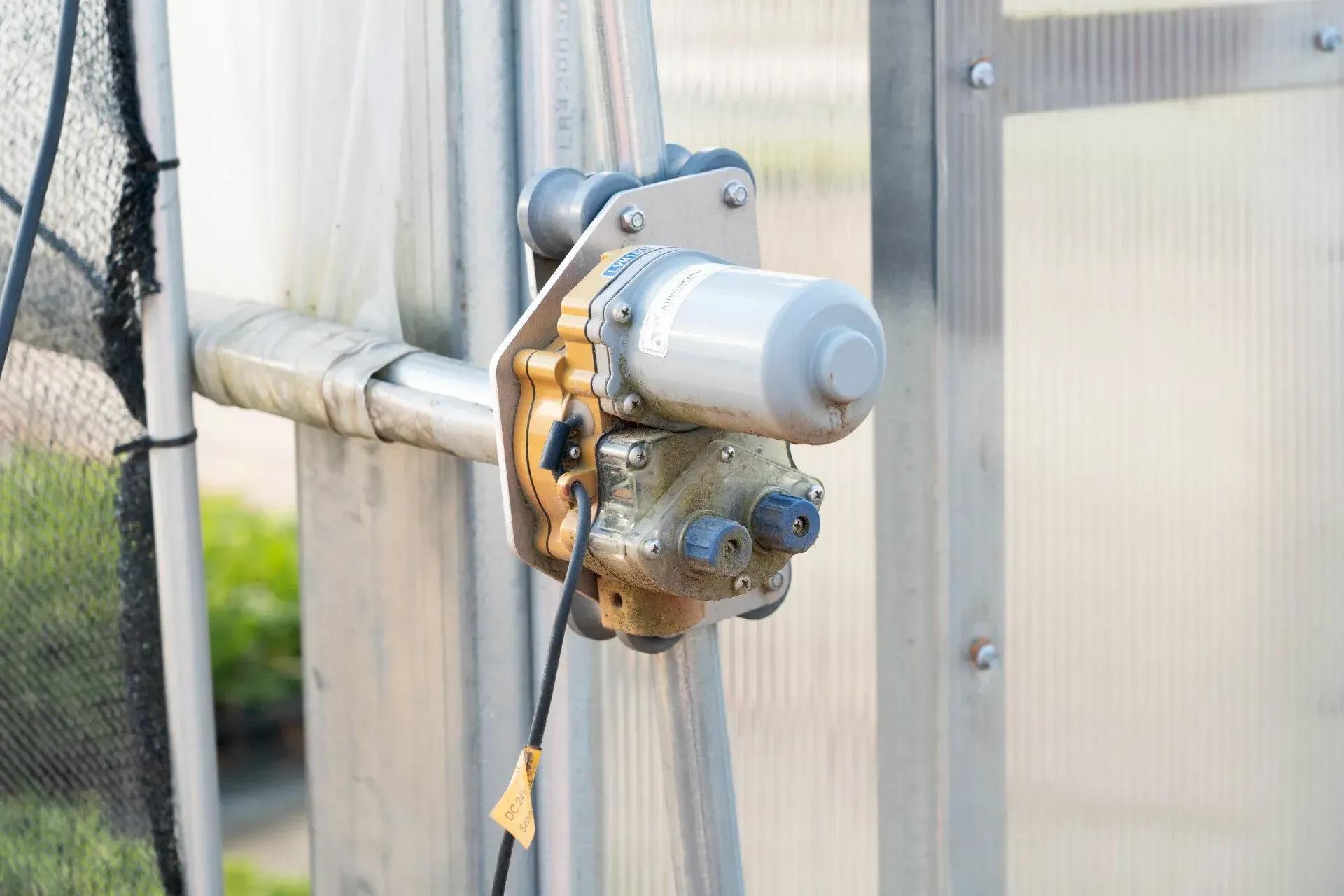 Motorized greenhouse vent opener attached to a metal frame. 