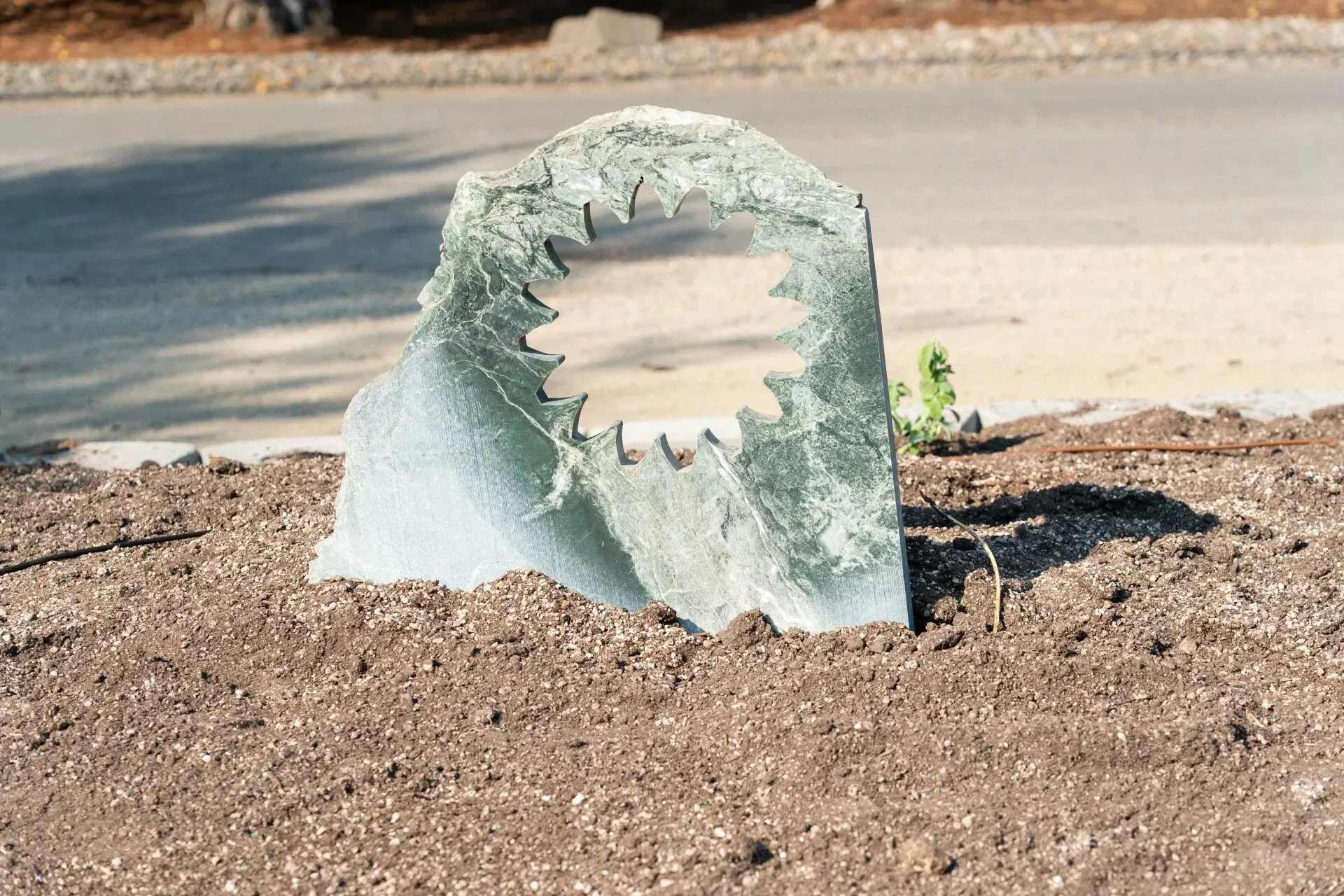 A green granite monument with a jagged opening, set in dirt by a road.