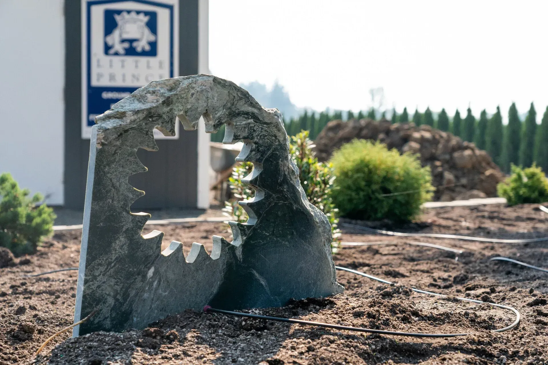 Stone sculpture with jagged teeth shape stands in a garden. The Little Prince sign is visible in the background.