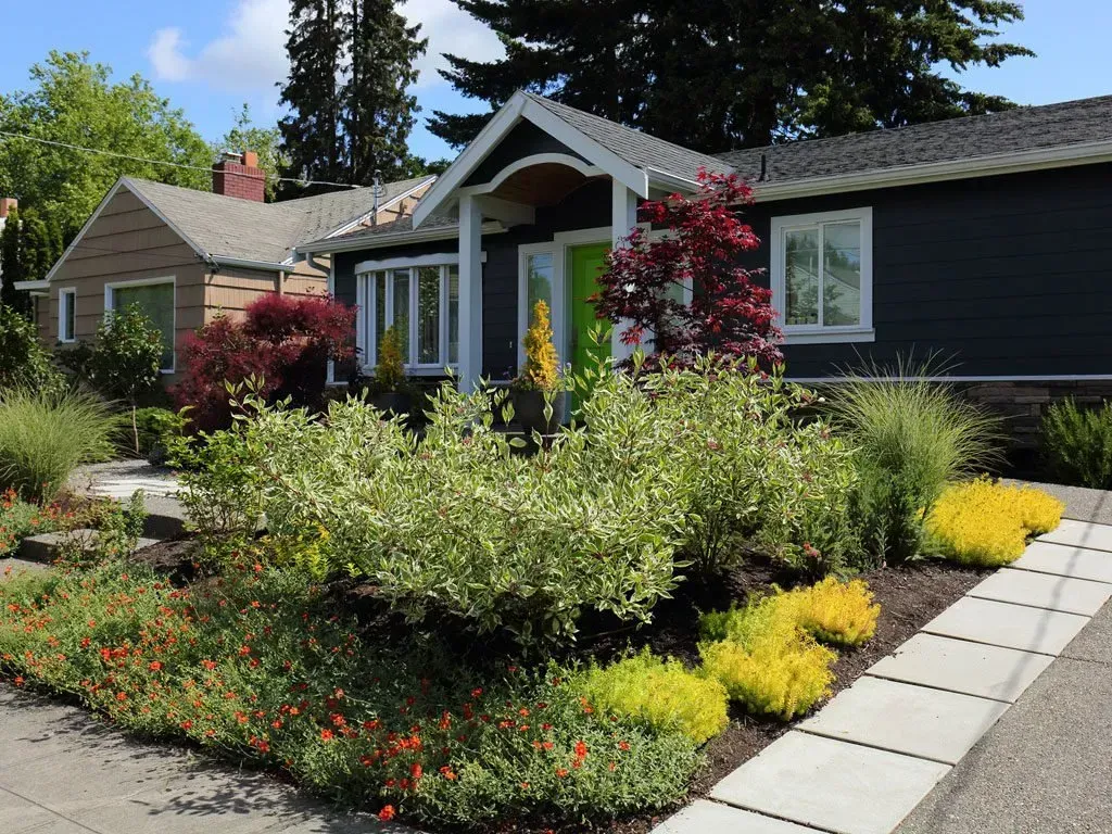 A dark blue house with a colorful garden in front. Yellow, red, and green plants line the walkway.