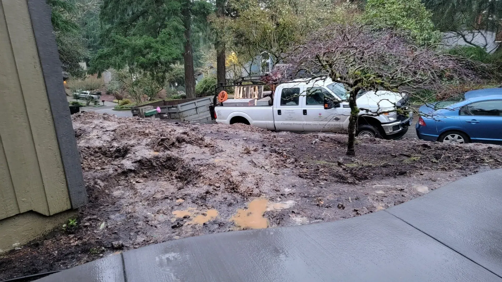 Mudslide engulfs a white pickup truck and blue car parked on a residential street, trees in the background.