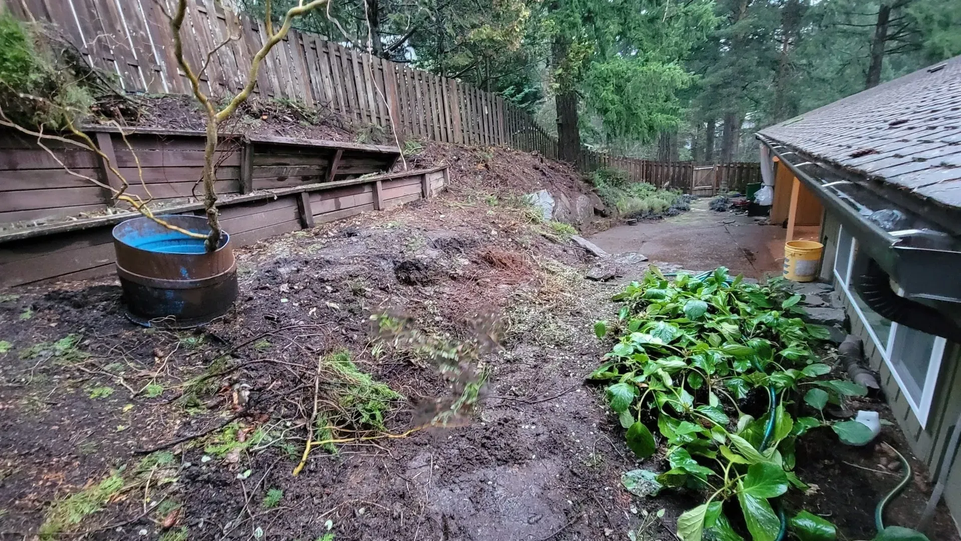 A muddy backyard with debris and a retaining wall.