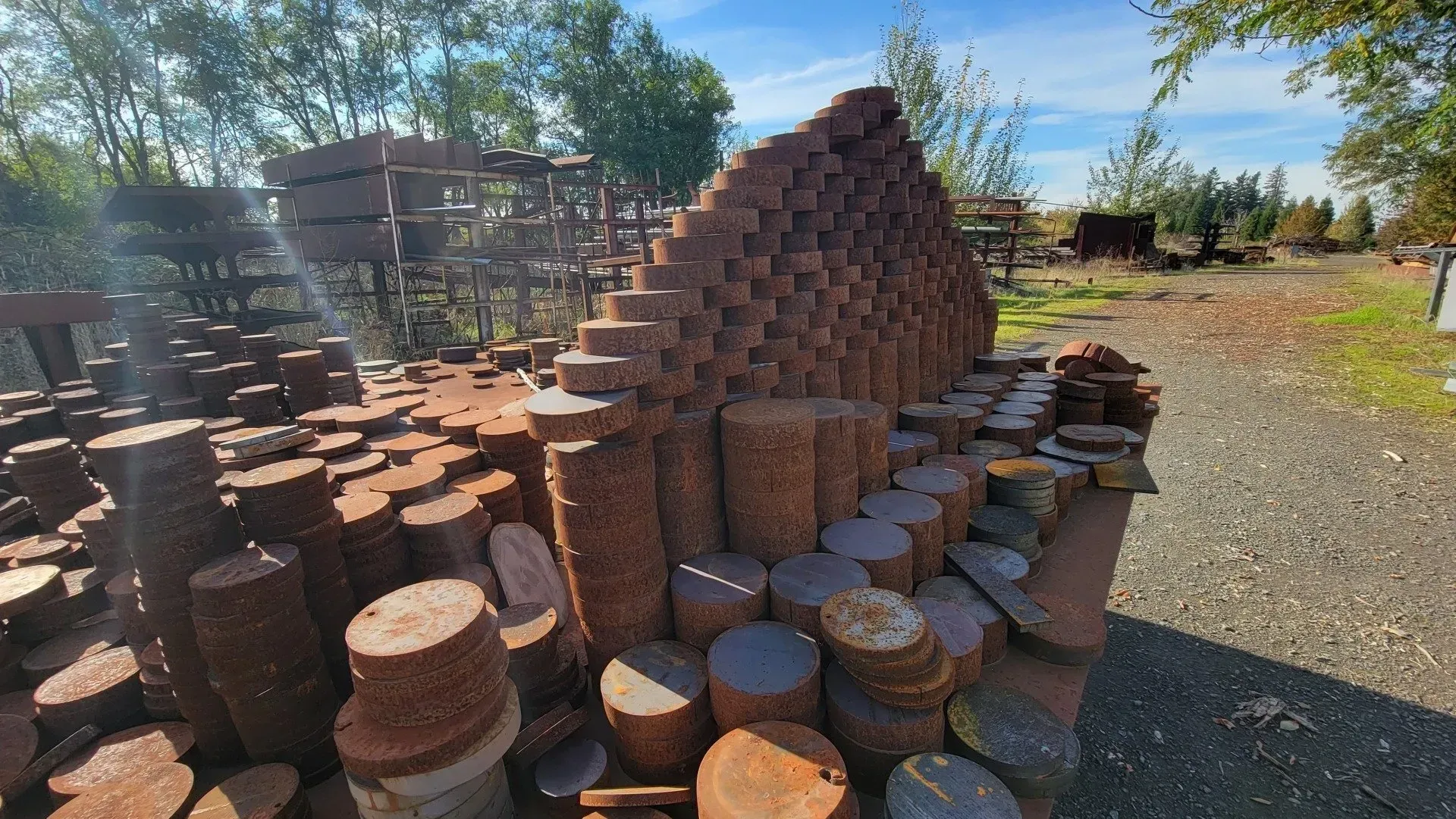 Sculpture made of stacked, cylindrical metal pieces in a sunlit outdoor setting. The rusted metal is brown and orange.