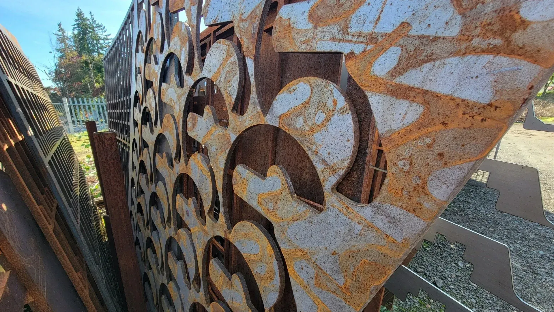 Rusty metal panels with cut-out patterns, possibly a fence or screen. Sunlight highlights the textures in an outdoor setting.
