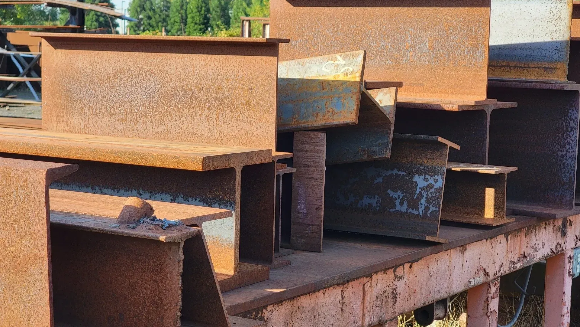 Rusty steel beams stacked on a metal surface, likely at a construction site or salvage yard.