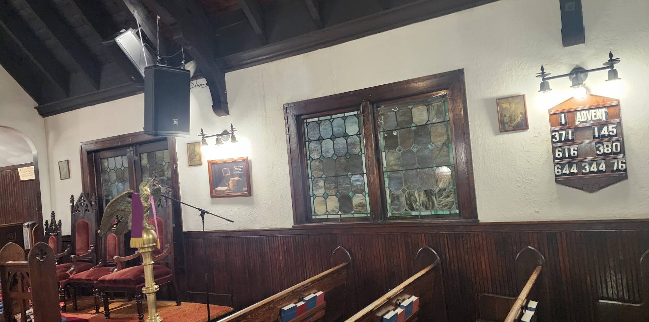 Interior view of a church with pews, stained glass windows, and a music speaker.