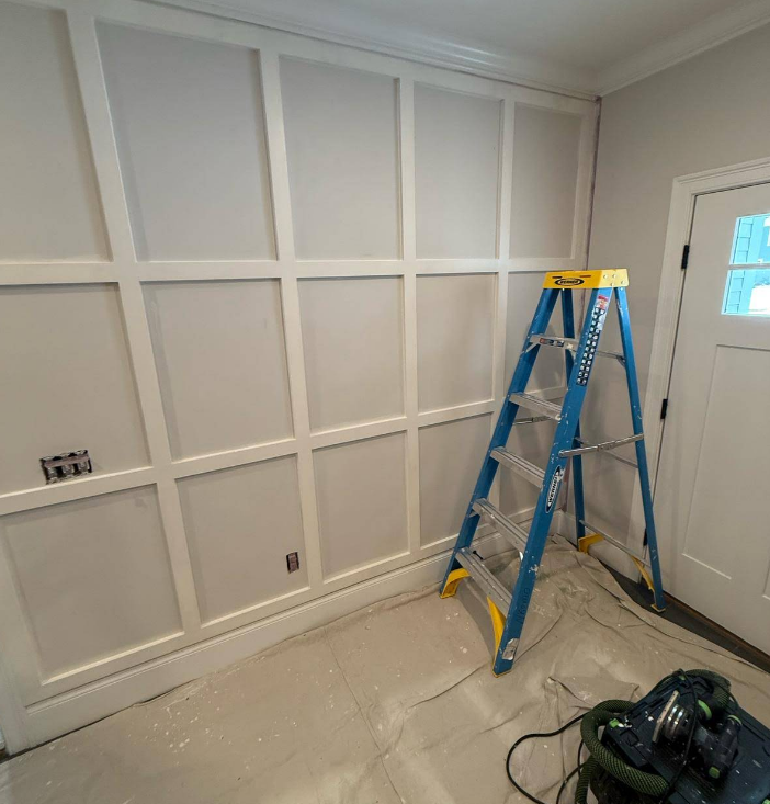 White paneled wall with a blue ladder and a door on the right.