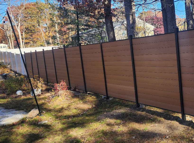 Brown horizontal slat fence with black posts, in a yard with trees and grass.