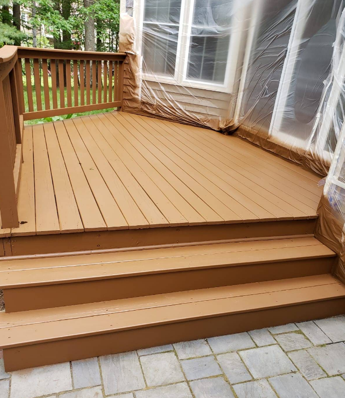 Brown painted deck with three steps leading to patio. Windows are covered in plastic sheeting.