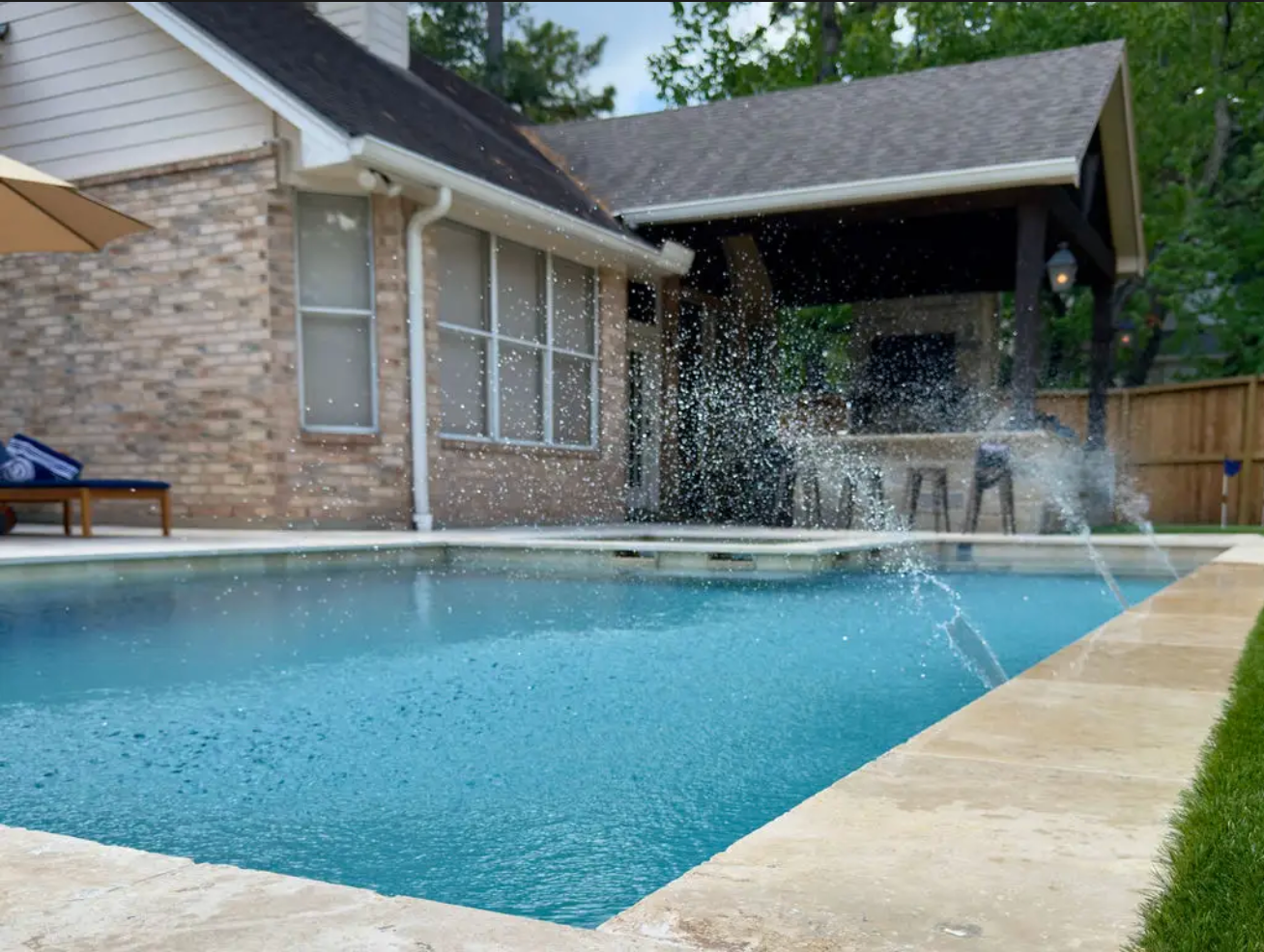 Pool with waterfall feature and built-in stone steps. Turquoise water, rock formation, and outdoor kitchen.