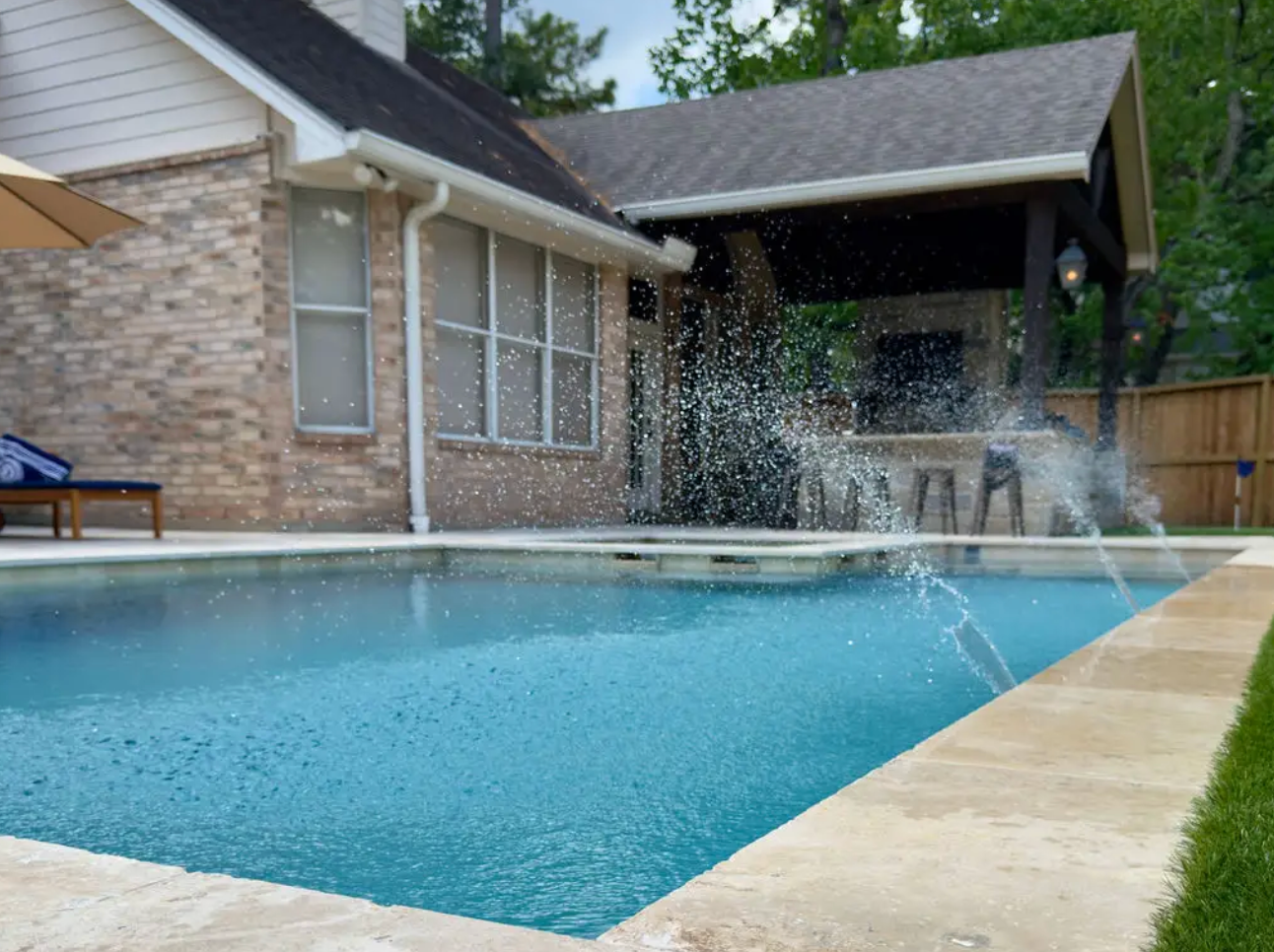 Overhead view of a pool with patio, lounge chairs, an umbrella, and landscaping.