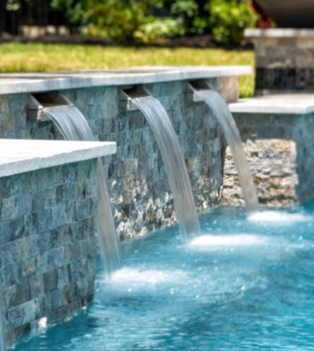 Pool with waterfall feature and built-in stone steps. Turquoise water, rock formation, and outdoor kitchen.