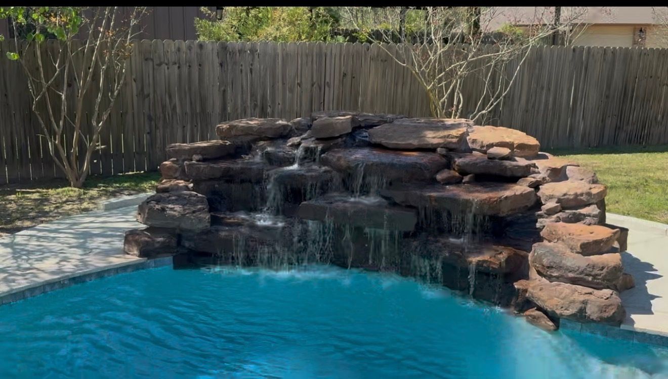Pool with waterfall feature and built-in stone steps. Turquoise water, rock formation, and outdoor kitchen.