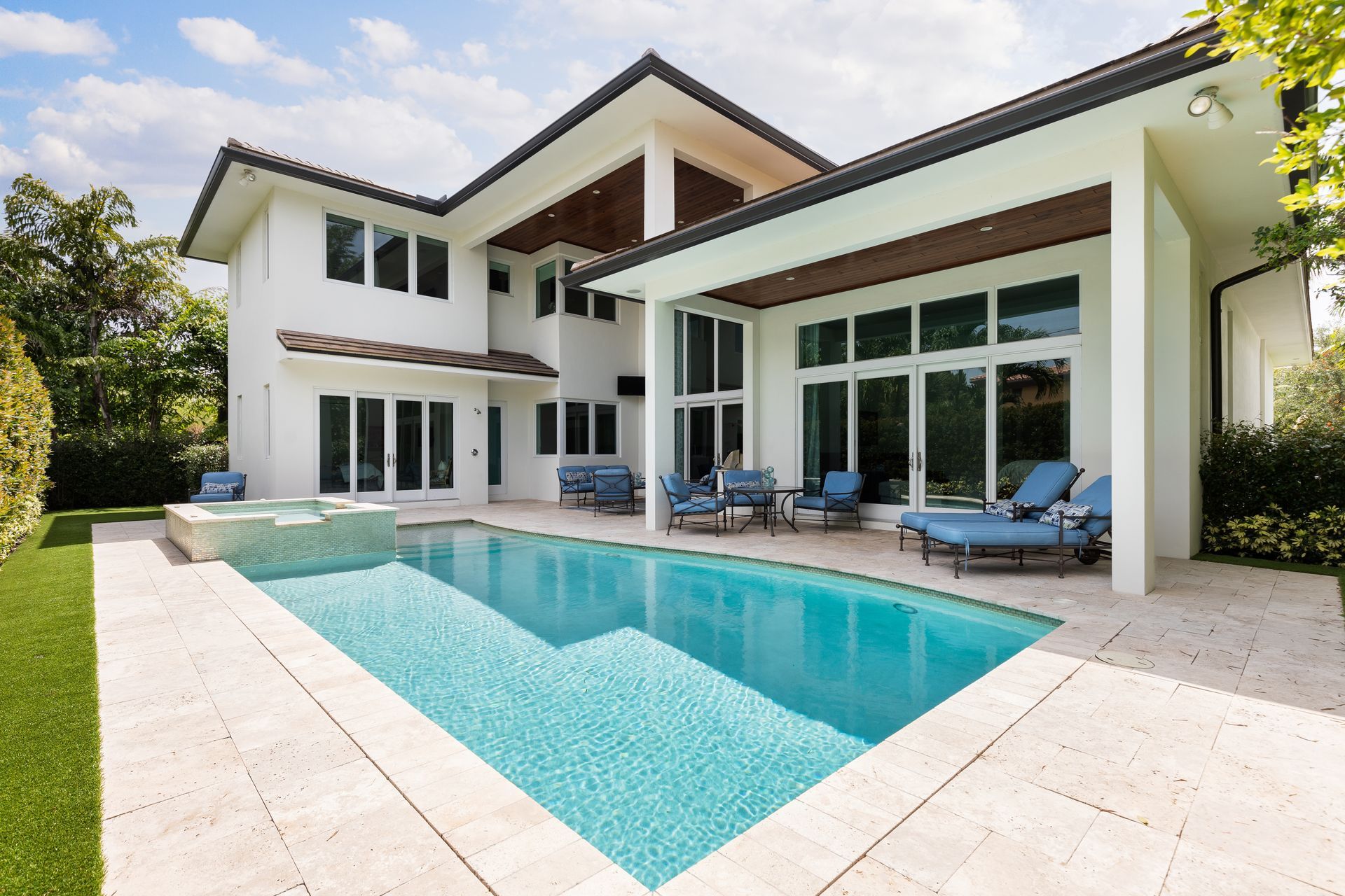 A modern two-story white house with a swimming pool and patio area surrounded by greenery under a blue sky.