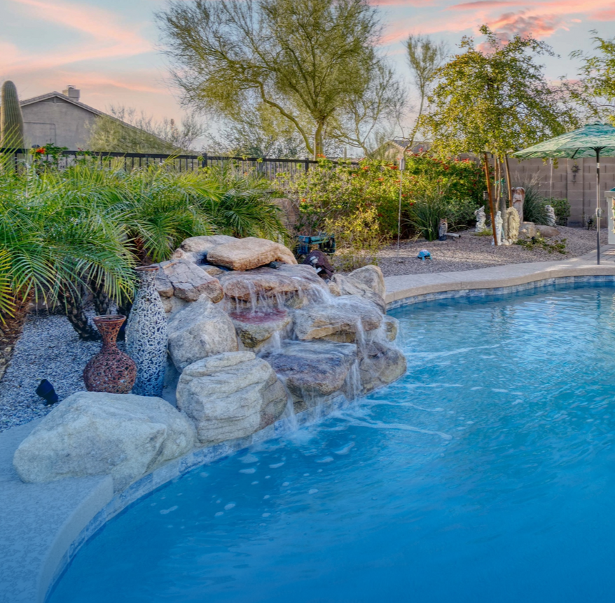 Overhead view of a pool with a light blue umbrella, lounge chairs, and a house with a gray roof.