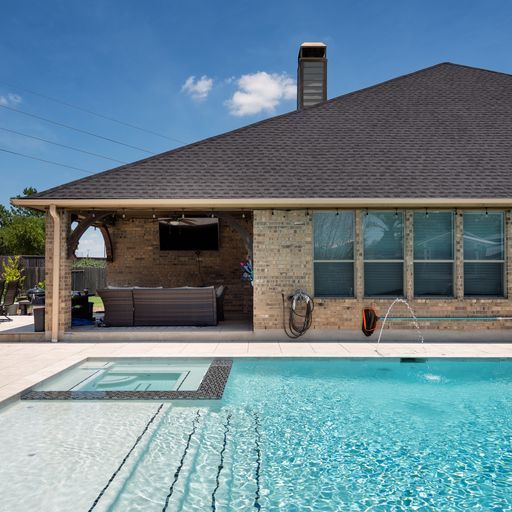 Outdoor pool with spa, waterfalls, patio furniture, and green grass.