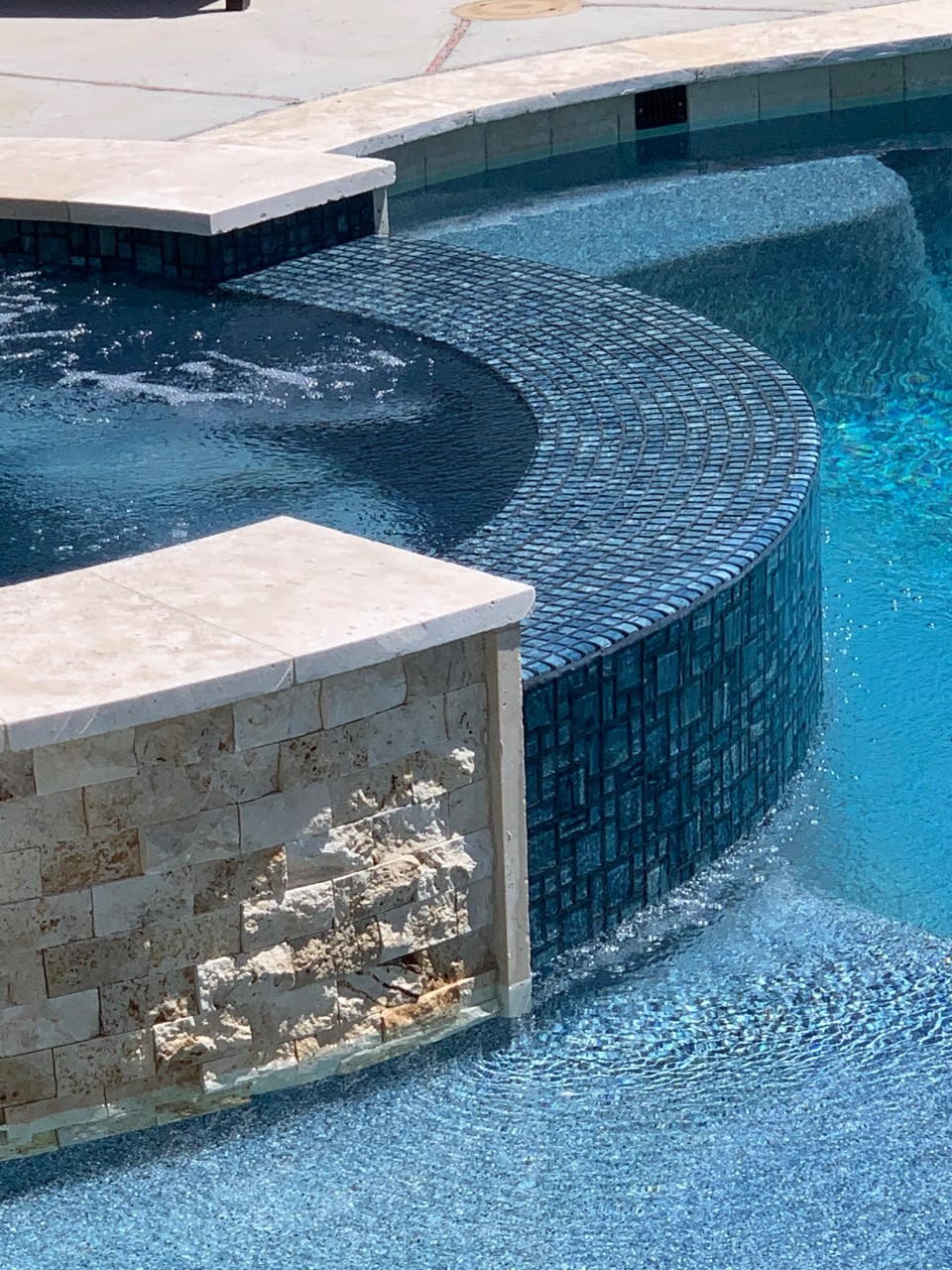 Pool and spa with cascading water feature; light stone, blue water.