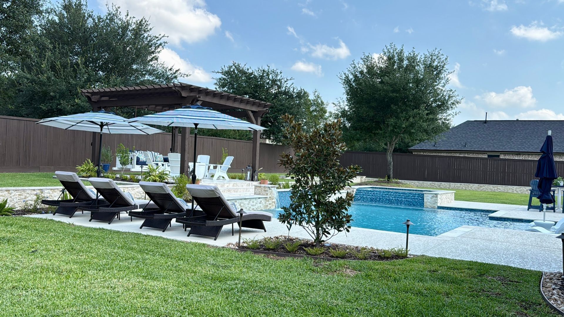 Hot tub and pool with landscaping. Blue water, beige decking, and green grass.