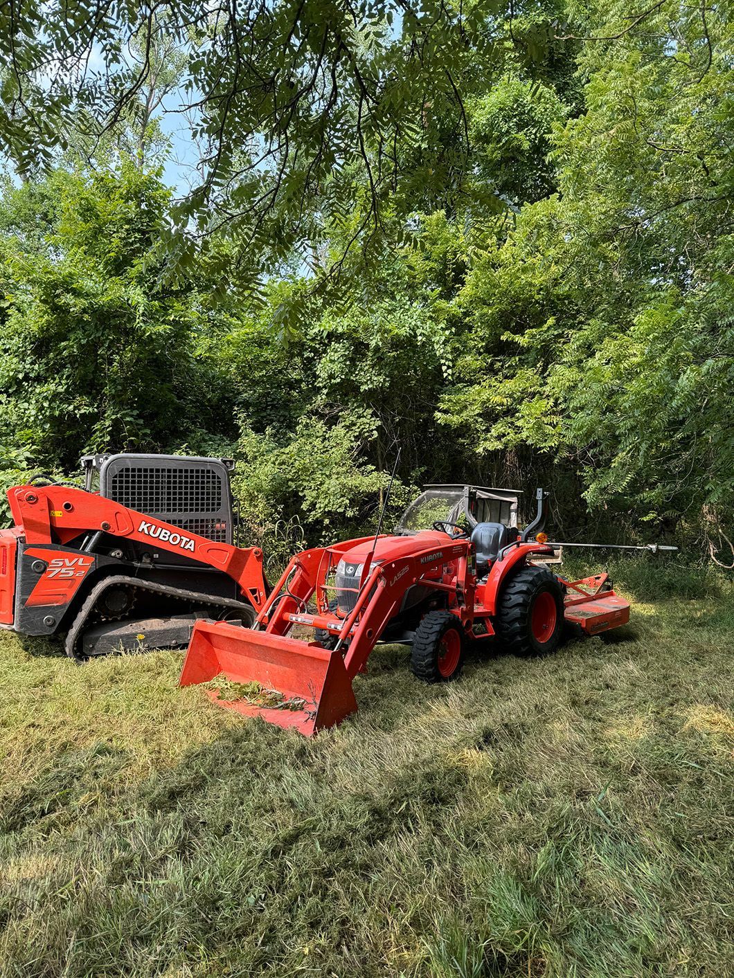 A tractor and a bulldozer are sitting in a field.