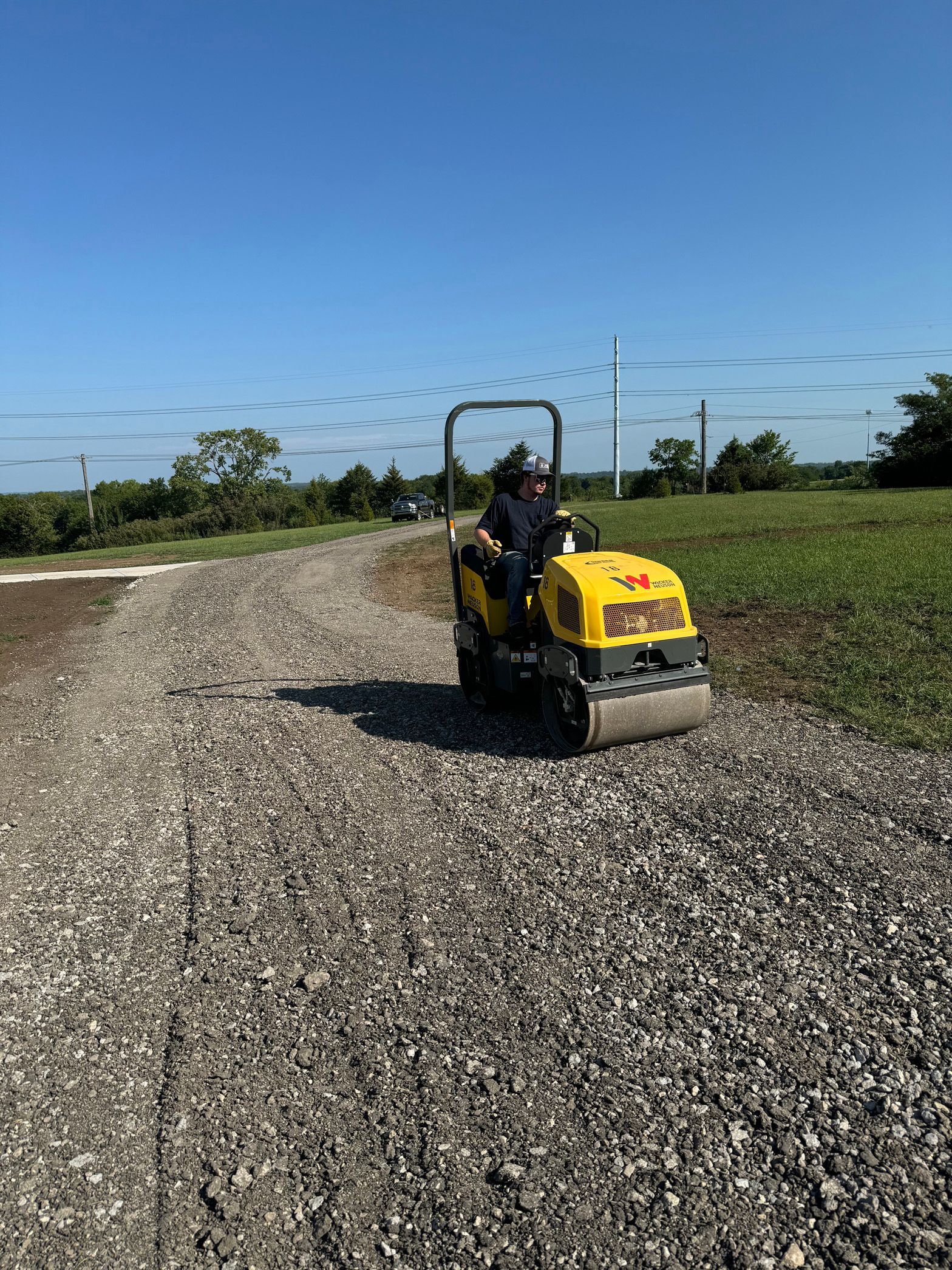 A man is driving a yellow roller on a gravel road.