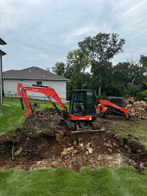 A couple of tractors are sitting on top of a dirt field in front of a house.