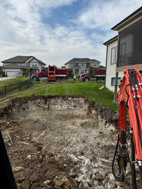 An excavator is digging a hole in the ground in front of a house.