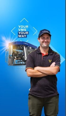 Smiling worker in a navy shirt and cap stands before a blue VMS sign reading “YOUR VMS YOUR WAY.”