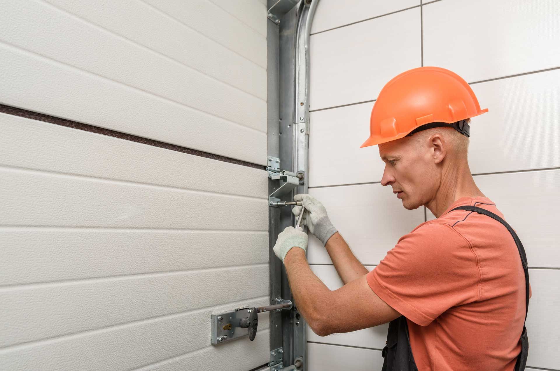 A man wearing a hard hat is working on a garage door.