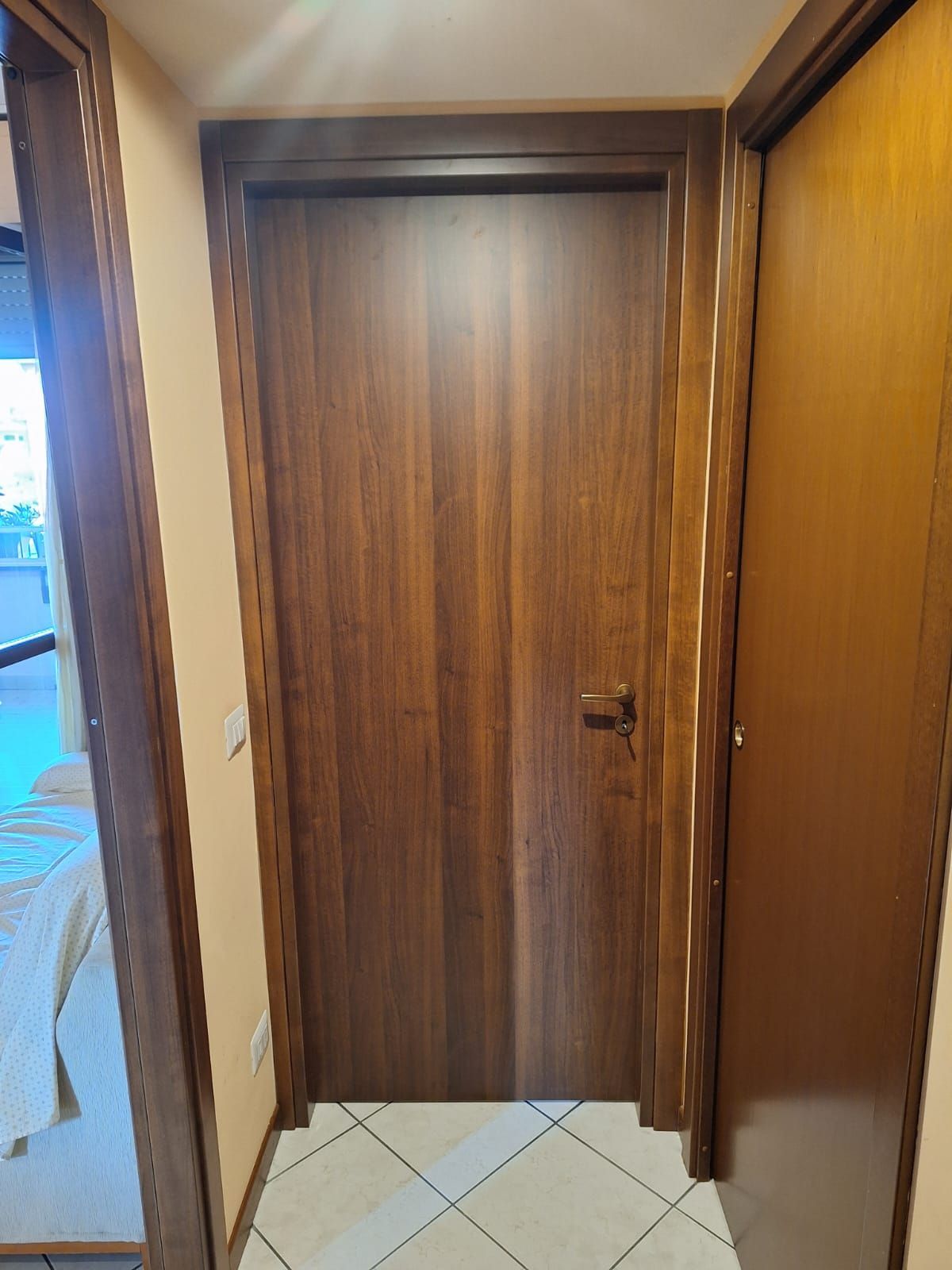 Porta in legno con telaio e maniglia marrone scuro, adiacente a una porta marrone più chiaro.