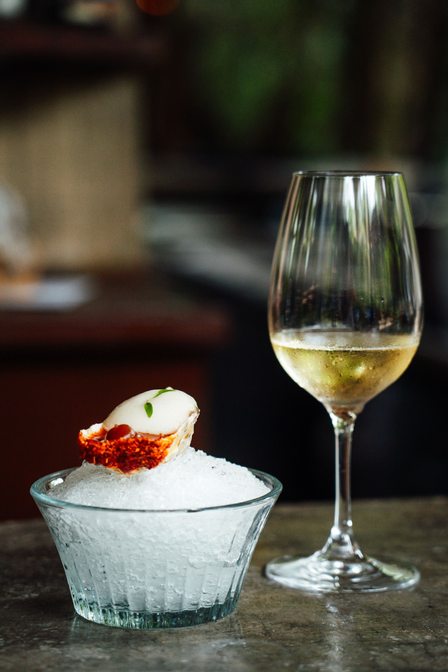A bowl of ice and an oyster and a glass of wine on a table.