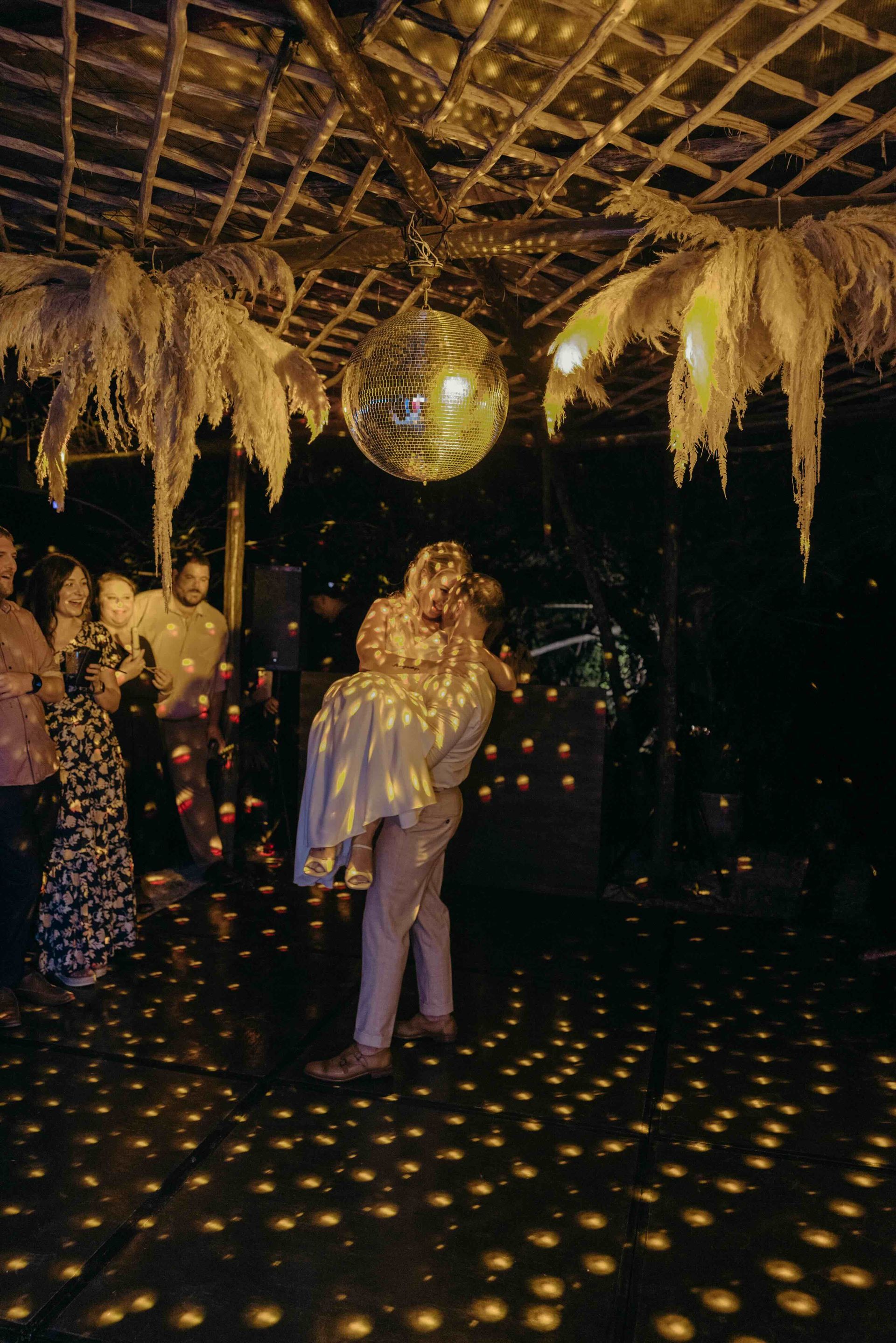 Man lifts woman in a dance at a party under a disco ball; warm lighting.