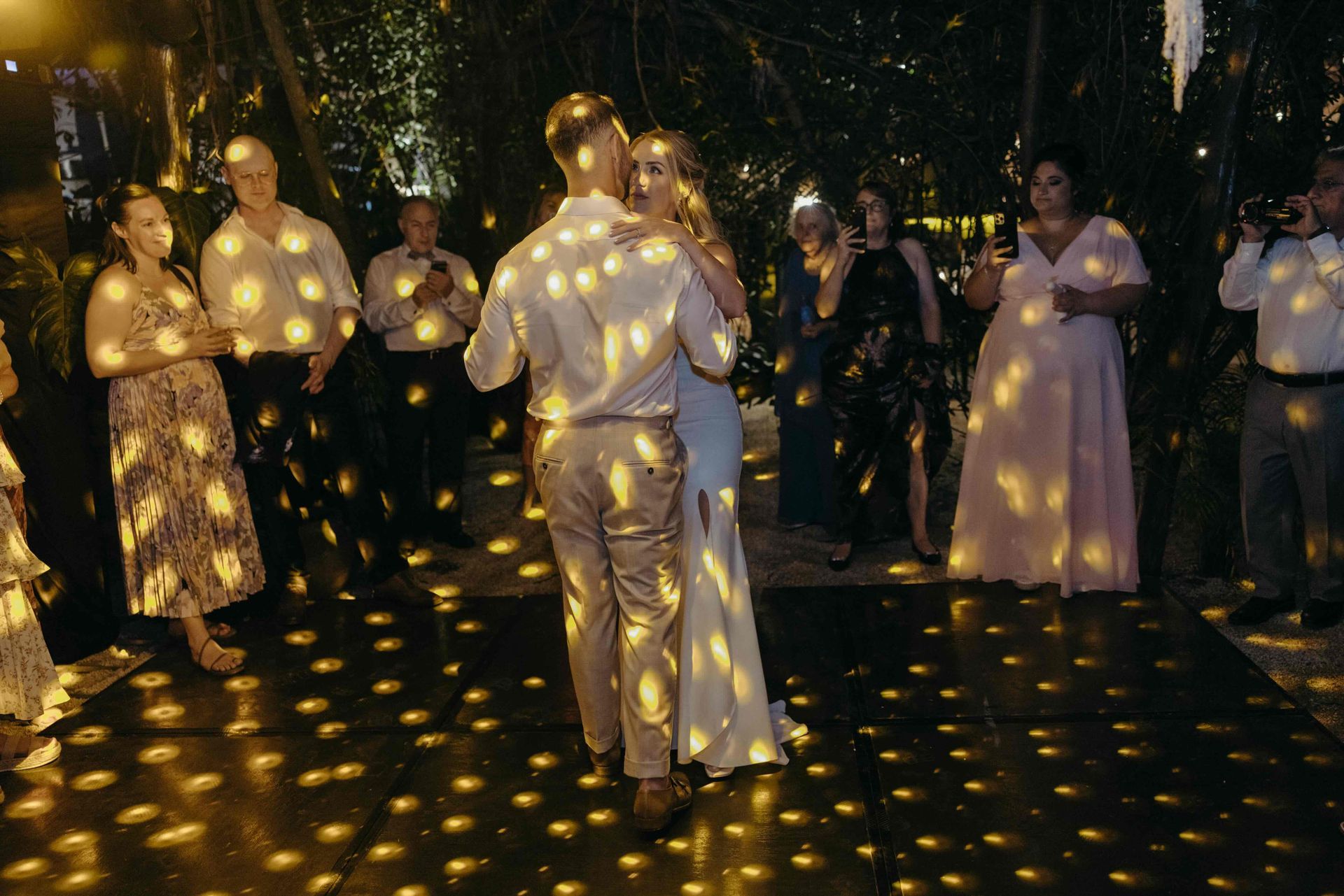 Couple dancing at wedding reception, illuminated by disco ball, guests watching.