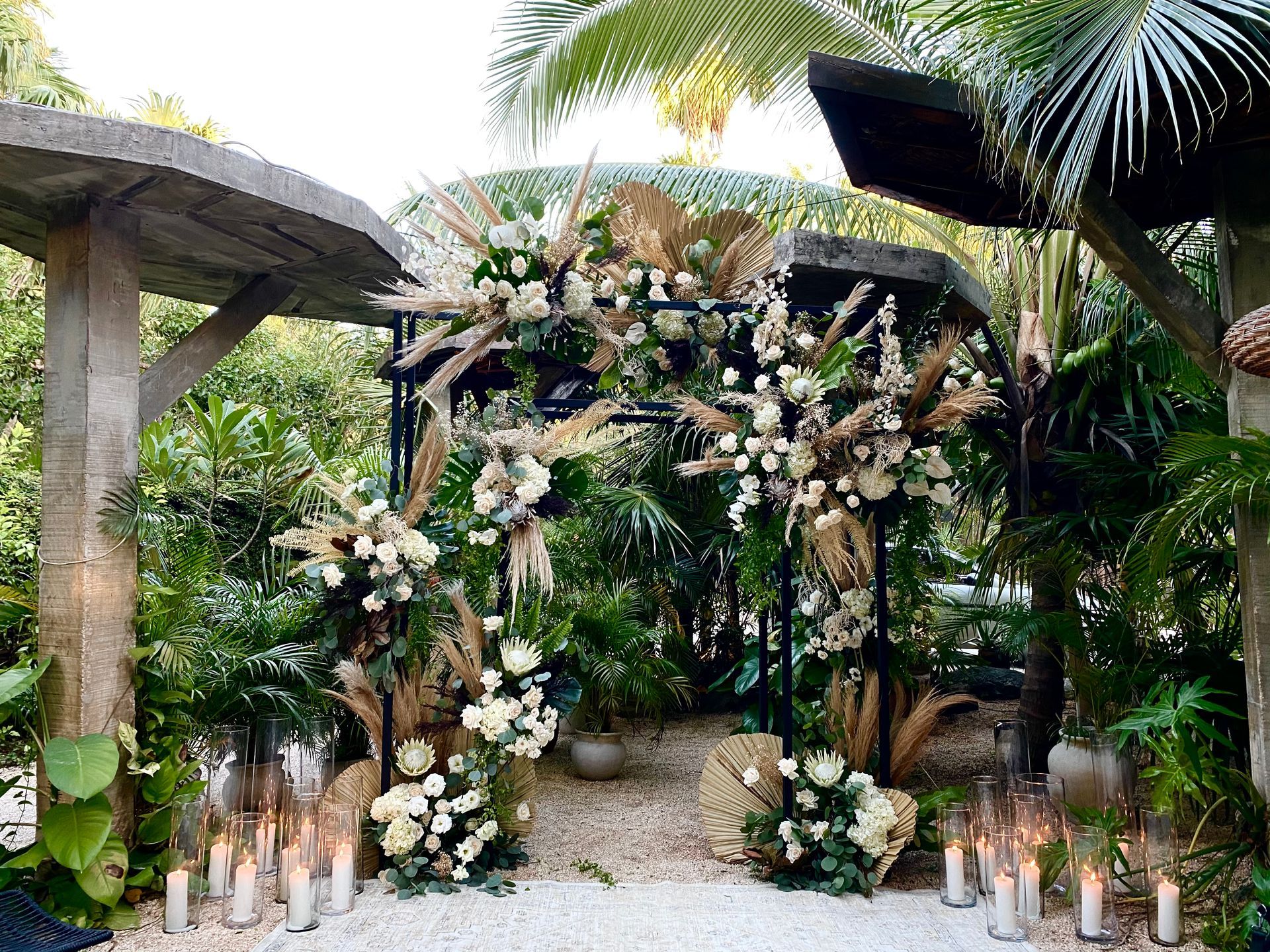 A wedding arch decorated with flowers and candles in a garden.