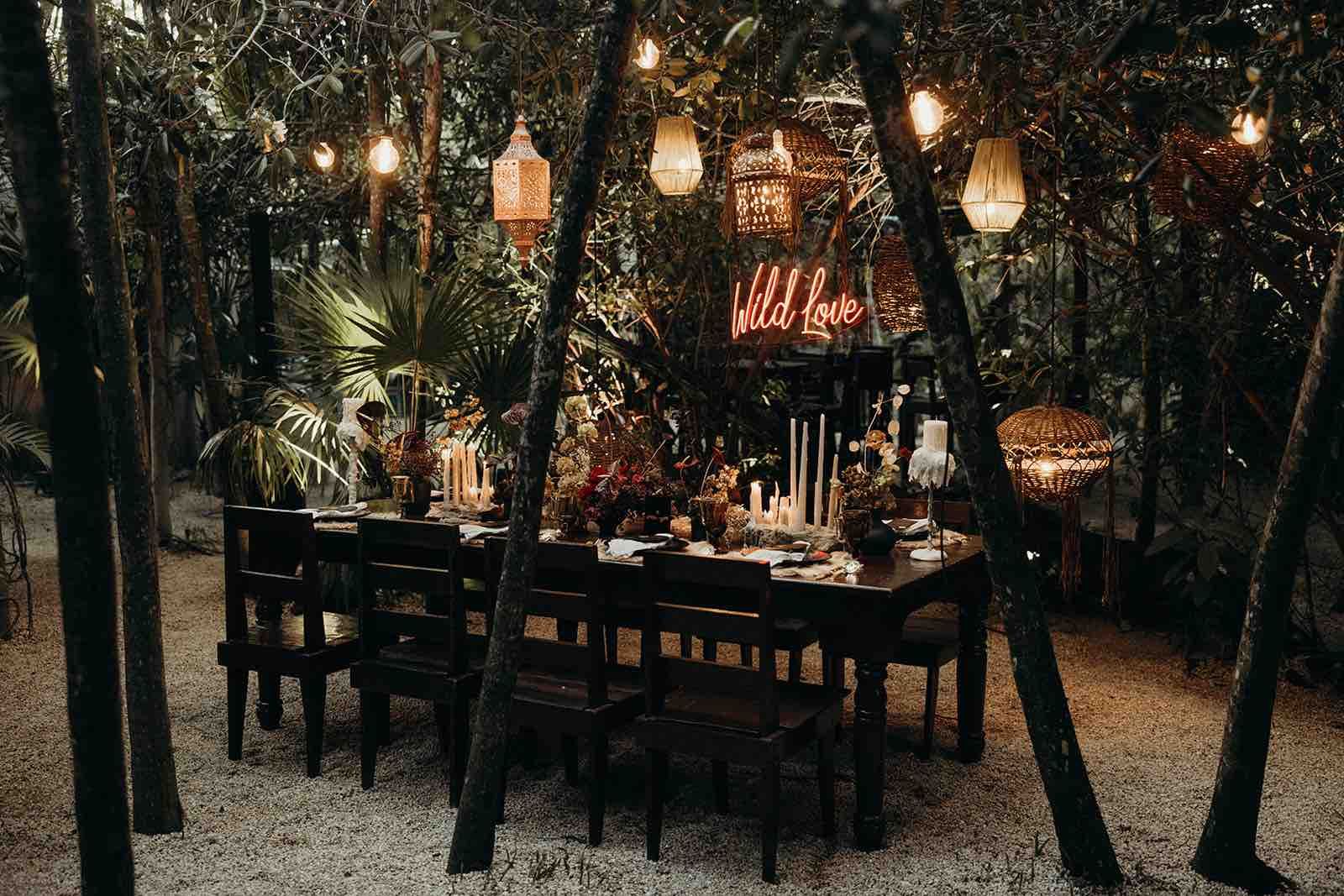A long table and chairs in the middle of a forest.