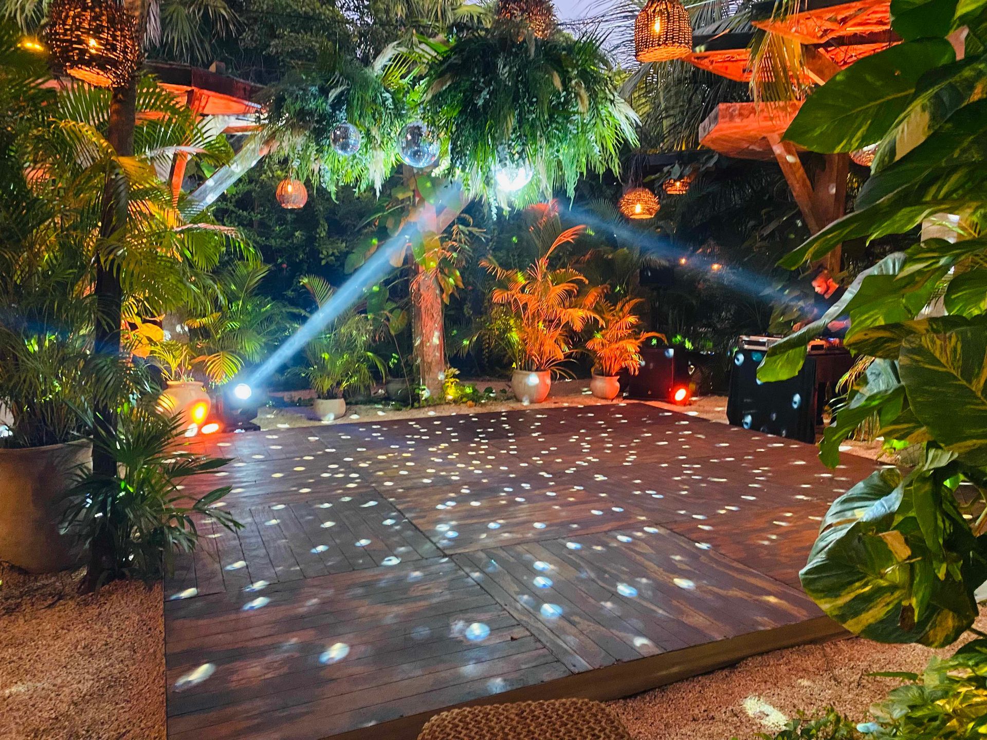 A wooden dance floor is surrounded by trees and plants at night at Wild Tulum
