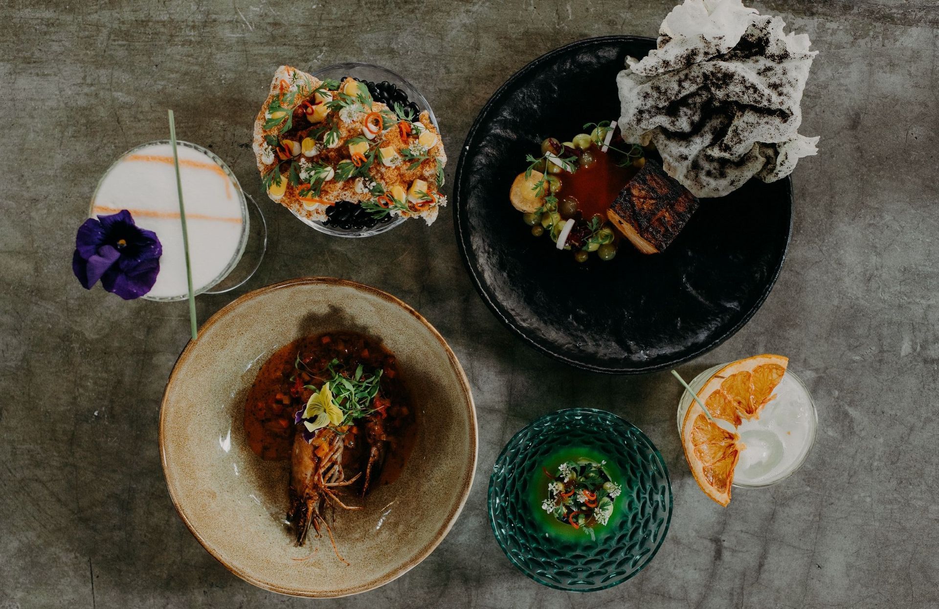 Assorted plated dishes and drinks arranged on a gray tabletop, viewed from above.
