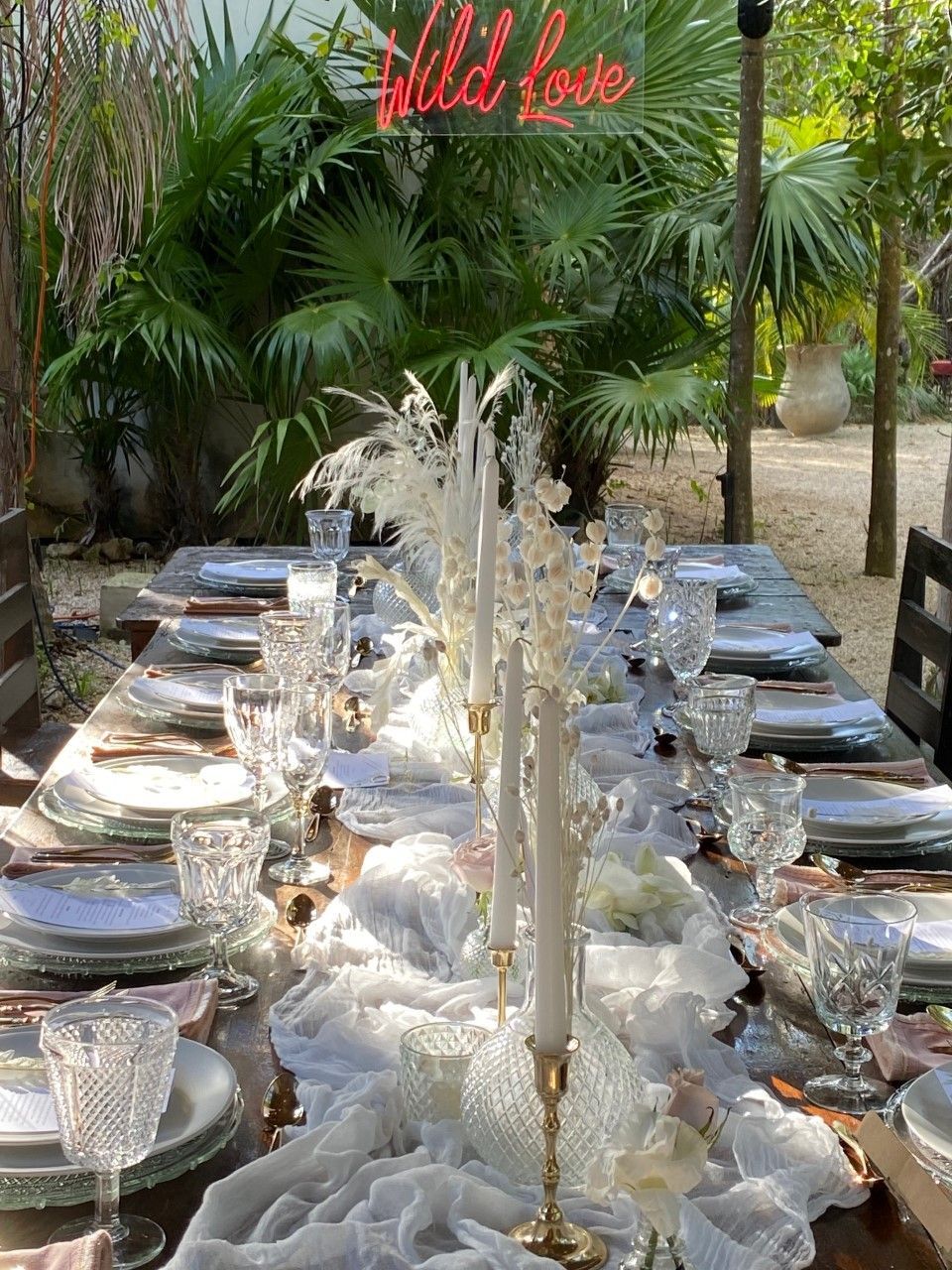 A long table with plates , glasses , candles and a neon sign that says `` wild love ''.
