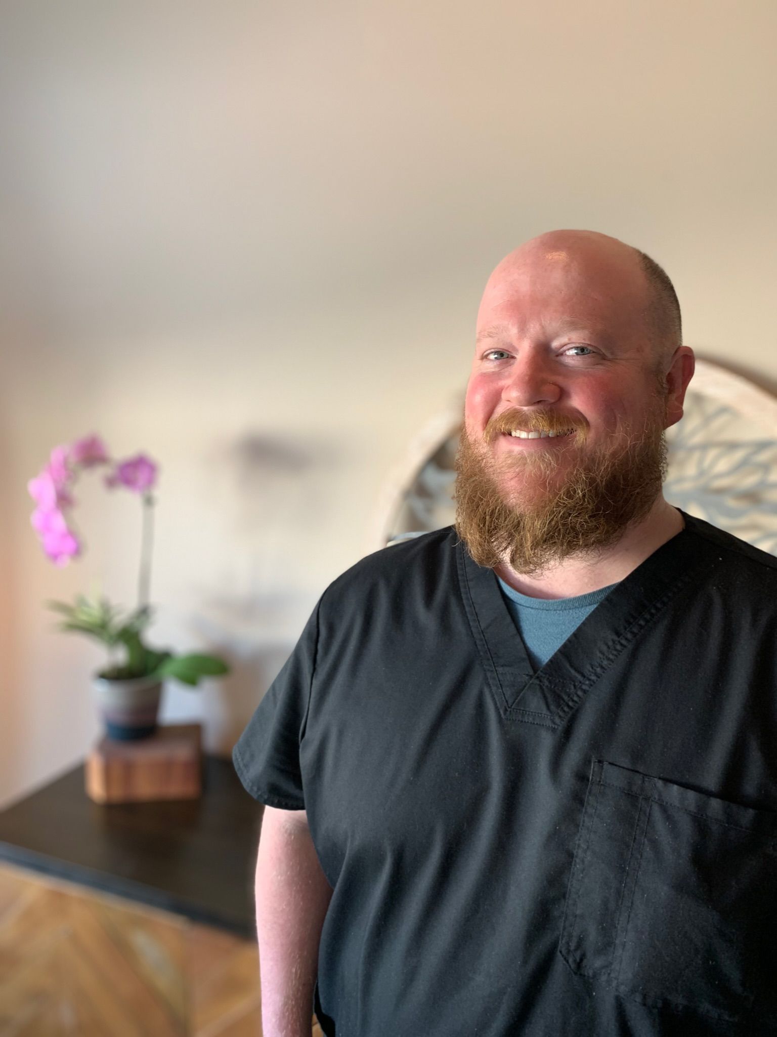 A man in a black scrub top is smiling for the camera.