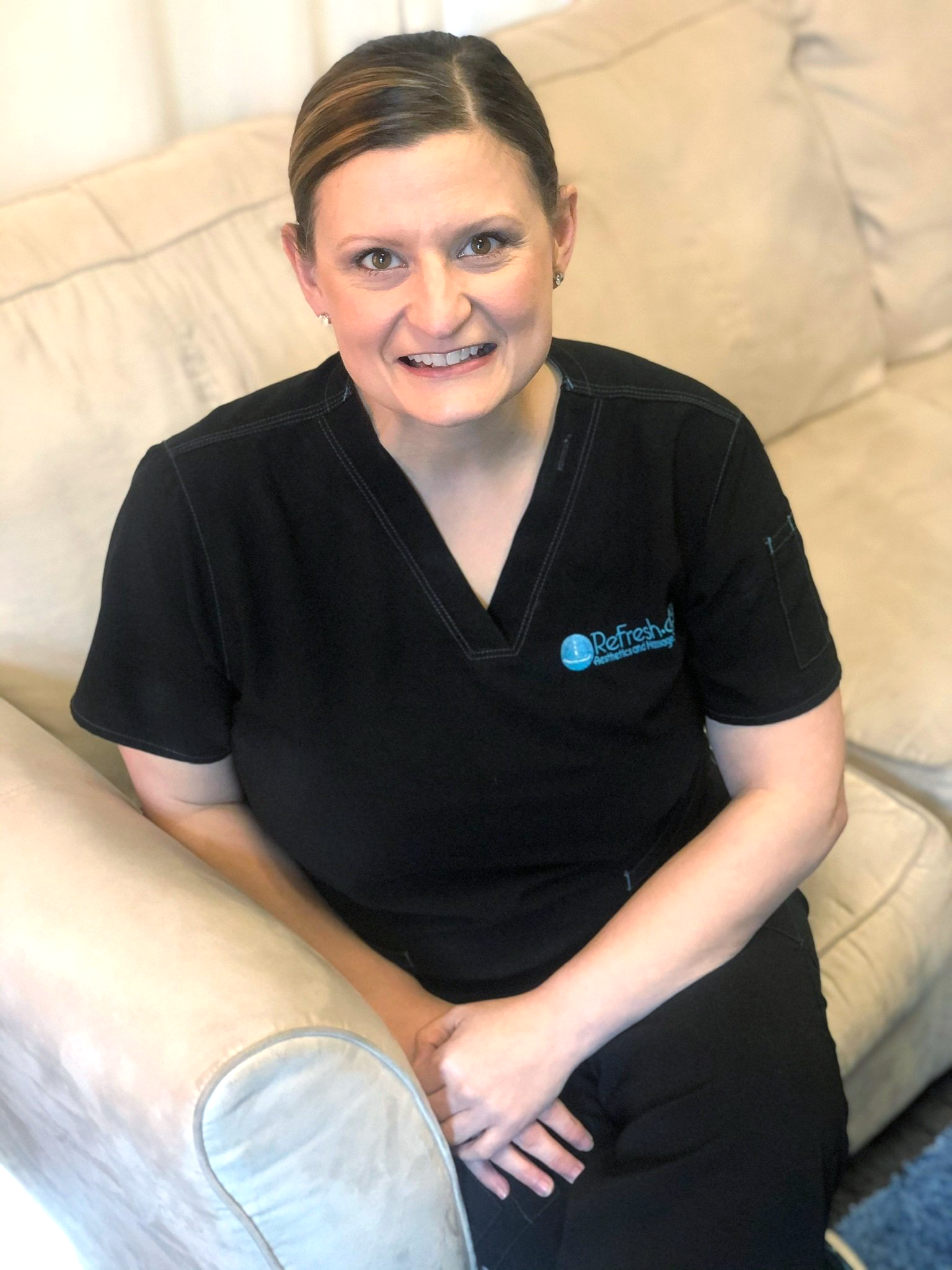 A woman is sitting on a couch wearing a black scrub top.