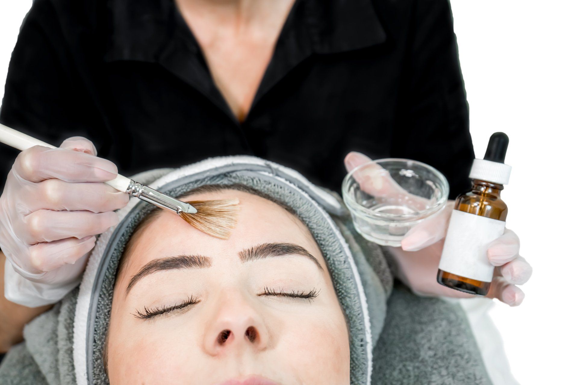 A woman is getting a facial treatment with a brush on her forehead.