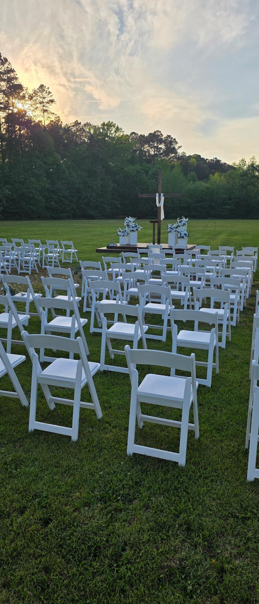 Rows of white folding chairs on grass in an open field at sunset, set up for an outdoor event