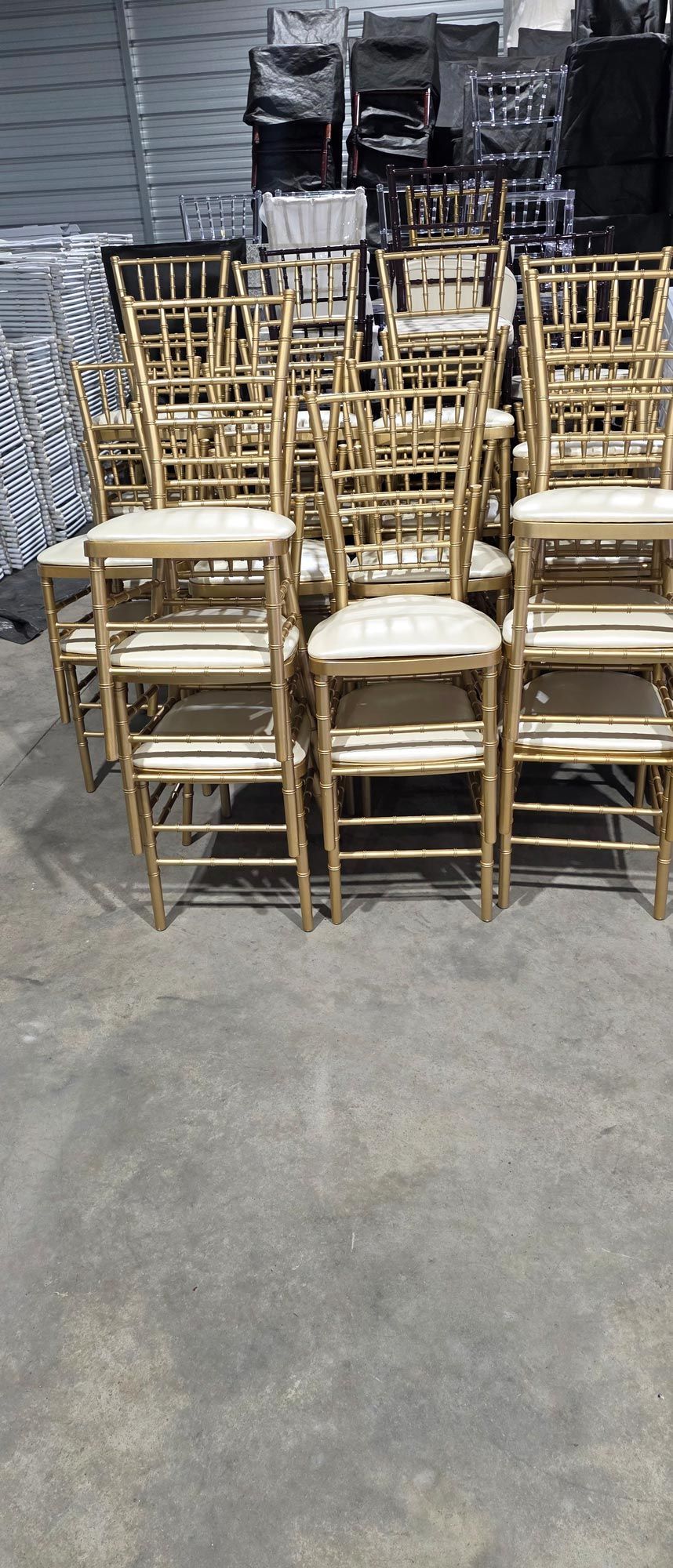 Stacked gold chairs and a few white chairs on a warehouse floor